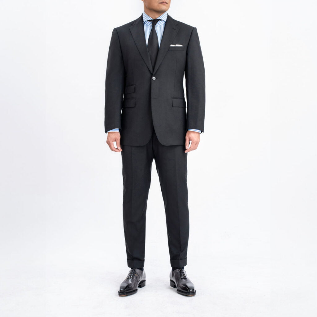 A man in a Black Suit, Sharkskin Wool, standing in front of a white background.