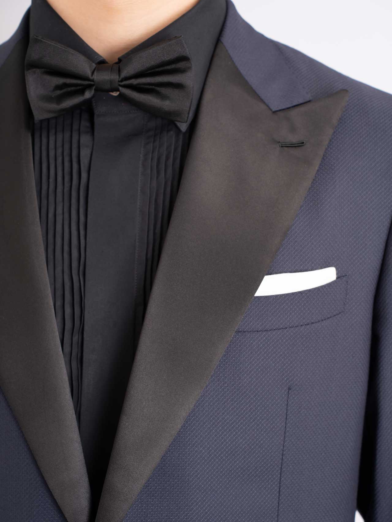 A man in a midnight blue tuxedo made of Australian wool/polyester with a black bow tie.