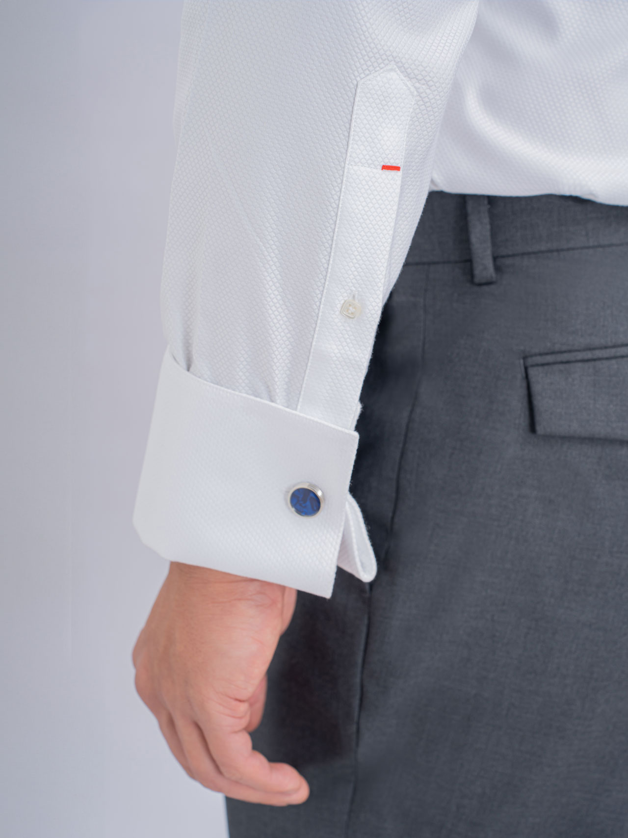 A man wearing a white smoking shirt and blue cufflinks, complementing his light blue suit.