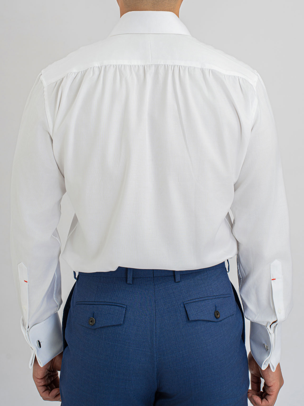 The back view of a man wearing a white shirt, collar TF88, Cotton 100s and blue pants with a cut away collar.