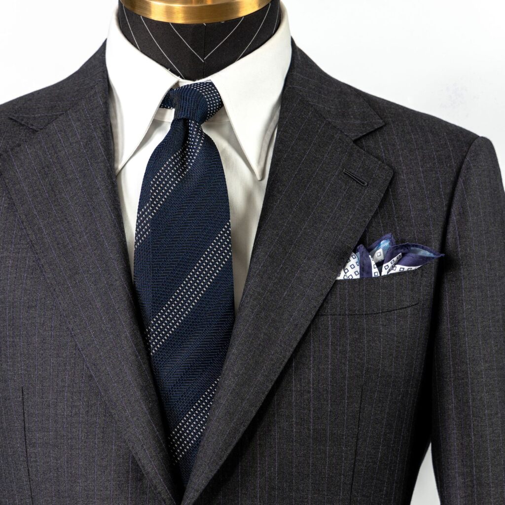 Close-up of a dark grey suit with a blue patterned tie and a matching pocket square.