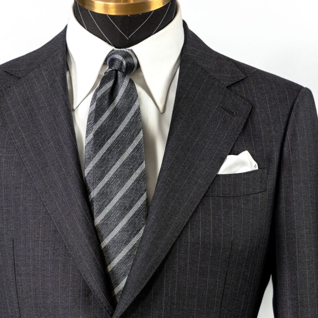 Close-up of a pinstriped suit jacket with a striped tie and pocket square.