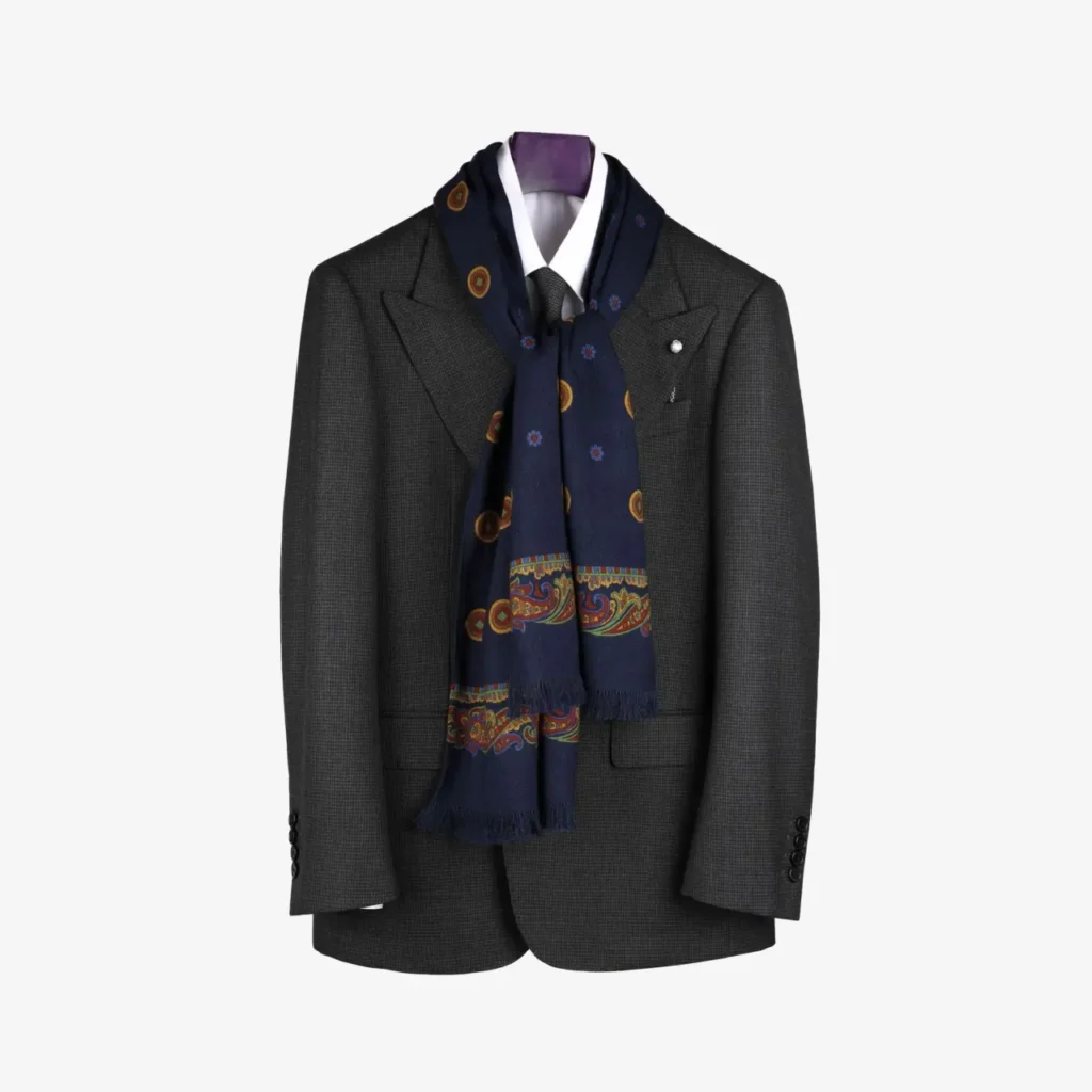 A dark gray suit jacket with a white dress shirt, accessorized with the Sarava – Wool and silk scarf in Navy draped stylishly around the collar.