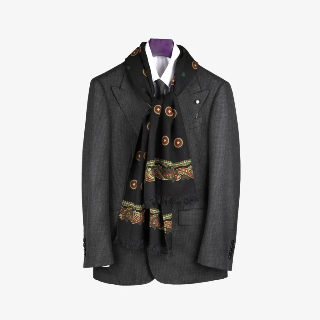A dark gray suit jacket with peak lapels is displayed on a hanger, complemented by the Sarava black wool and silk scarf featuring circular and paisley patterns.