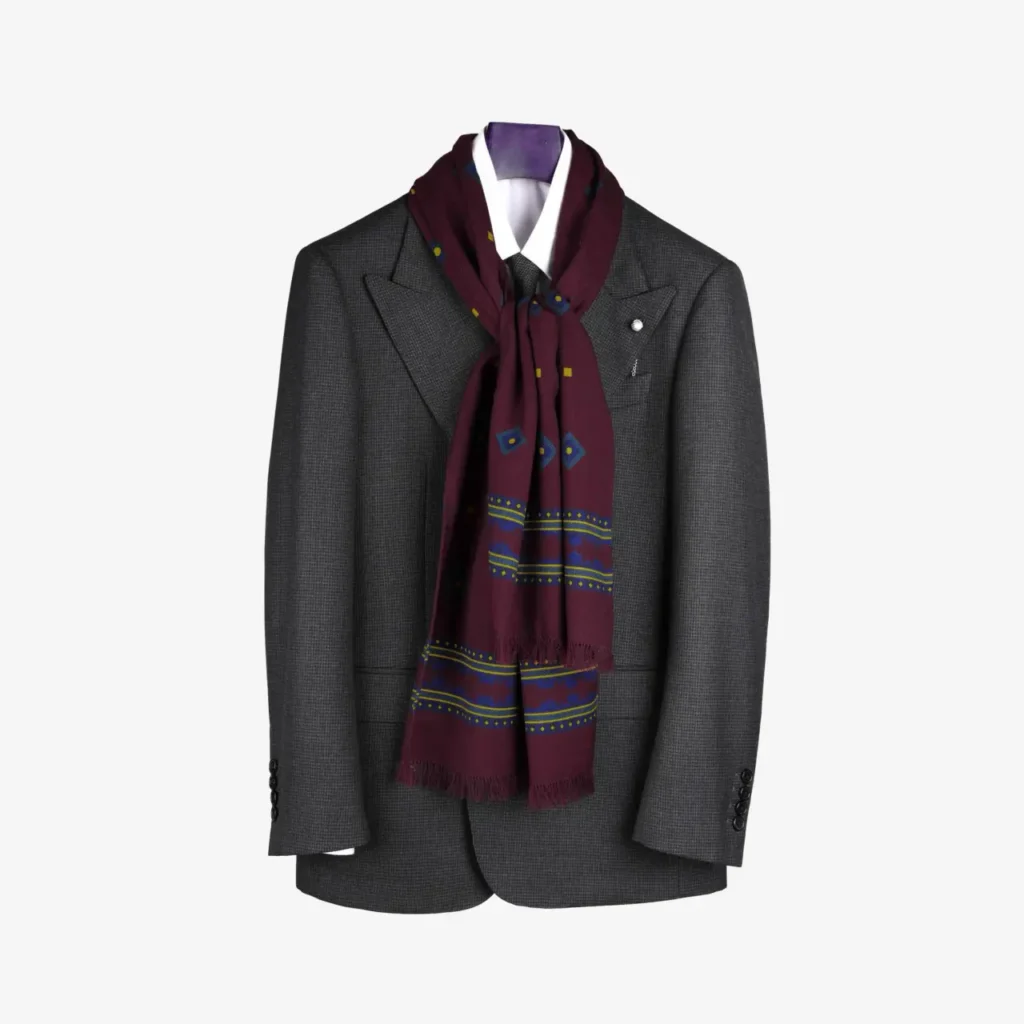 A charcoal gray suit jacket on a mannequin, styled with a white shirt, black tie, and the Kandora – Wool and Silk Scarf in Burgundy draped elegantly around the collar.