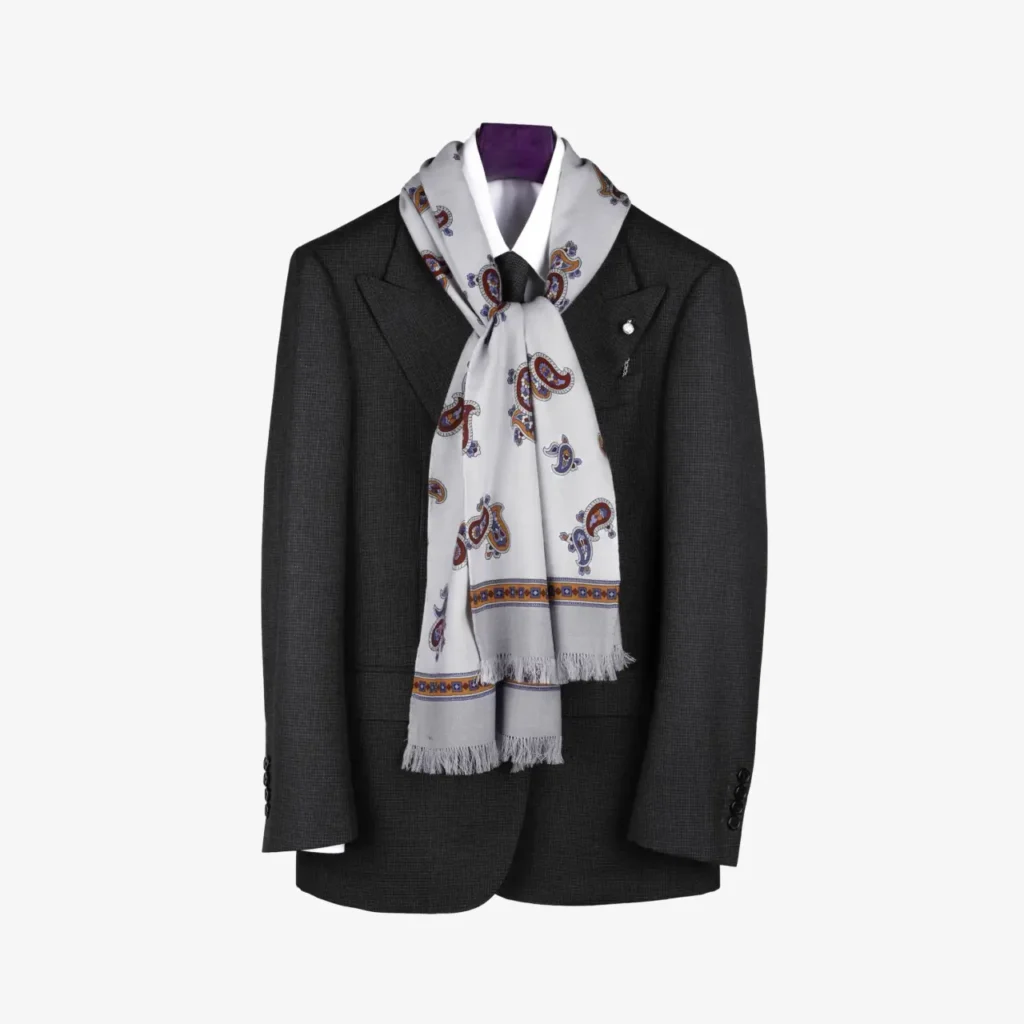 A dark suit jacket on a hanger with the Fidema – Wool and silk scarf, Light grey, featuring a paisley pattern, draped around the collar.