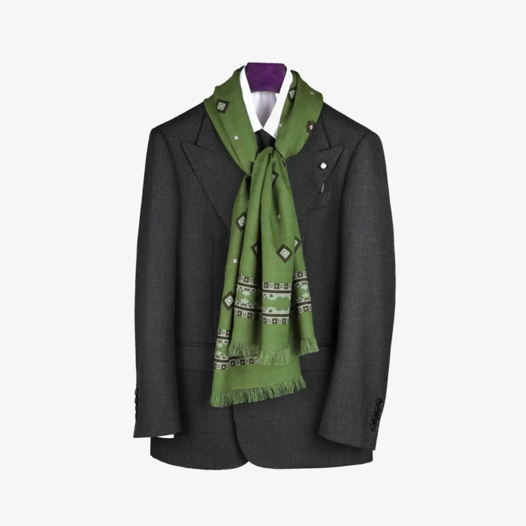 A dark gray suit jacket on a hanger with a white shirt and the Kandora – Wool and Silk Scarf in Forest Green elegantly draped around the collar.
