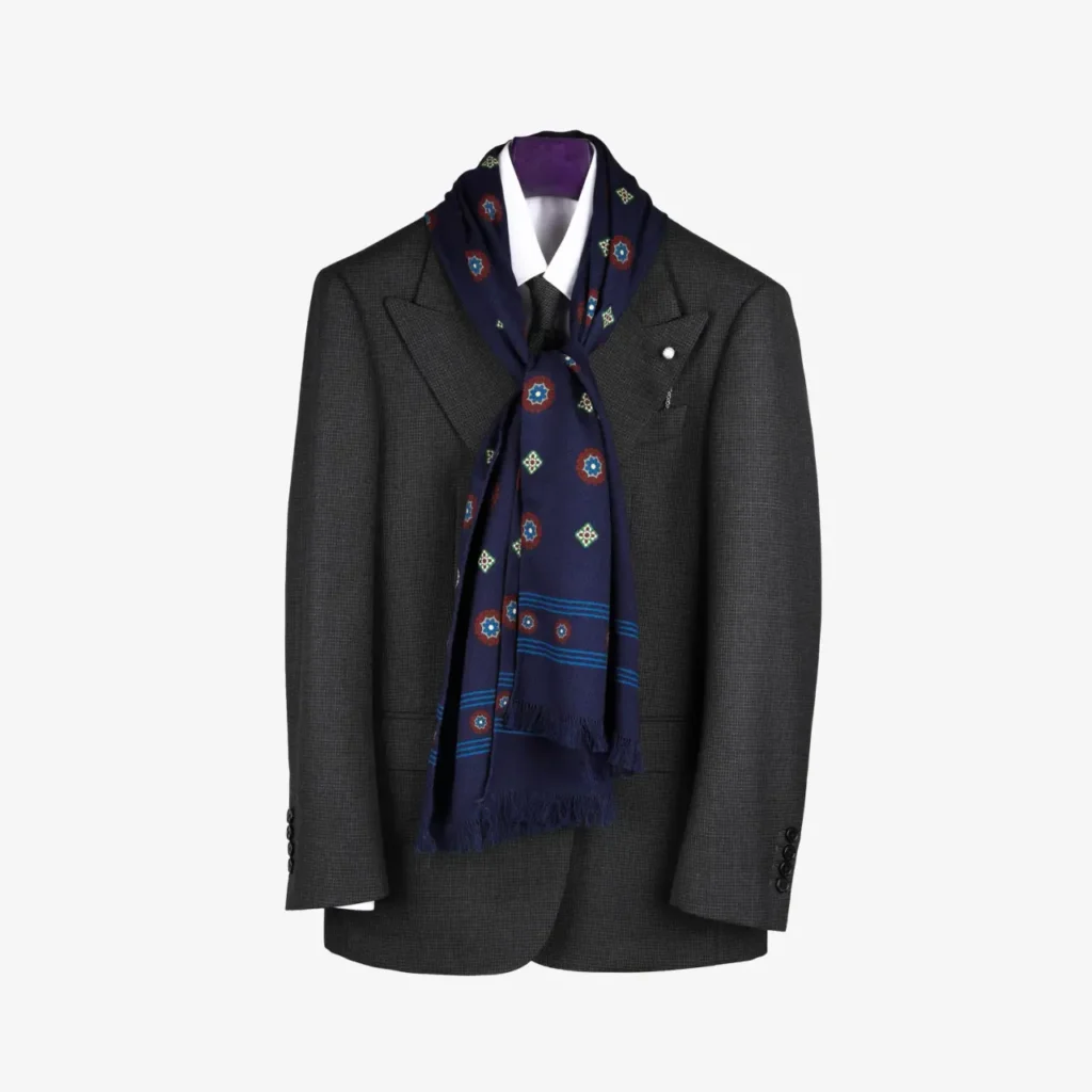 A dark gray suit jacket on a hanger with a white shirt, black tie, and the Lunema – Wool and silk scarf in Midnight blue elegantly draped around the collar.