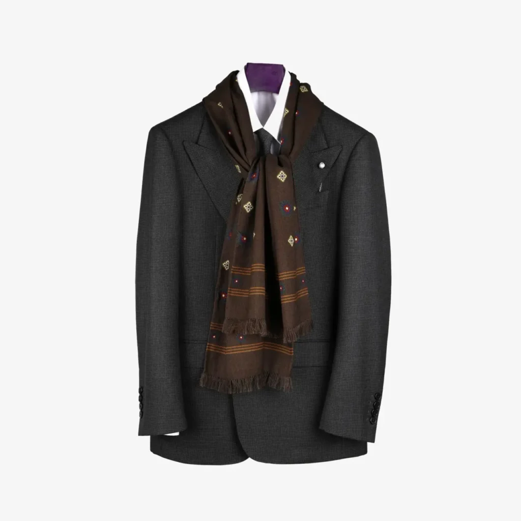 A charcoal grey suit jacket hangs on a hanger, styled with a crisp white shirt and the Lunema – Wool and silk scarf in Midnight blue, draped elegantly around the collar.