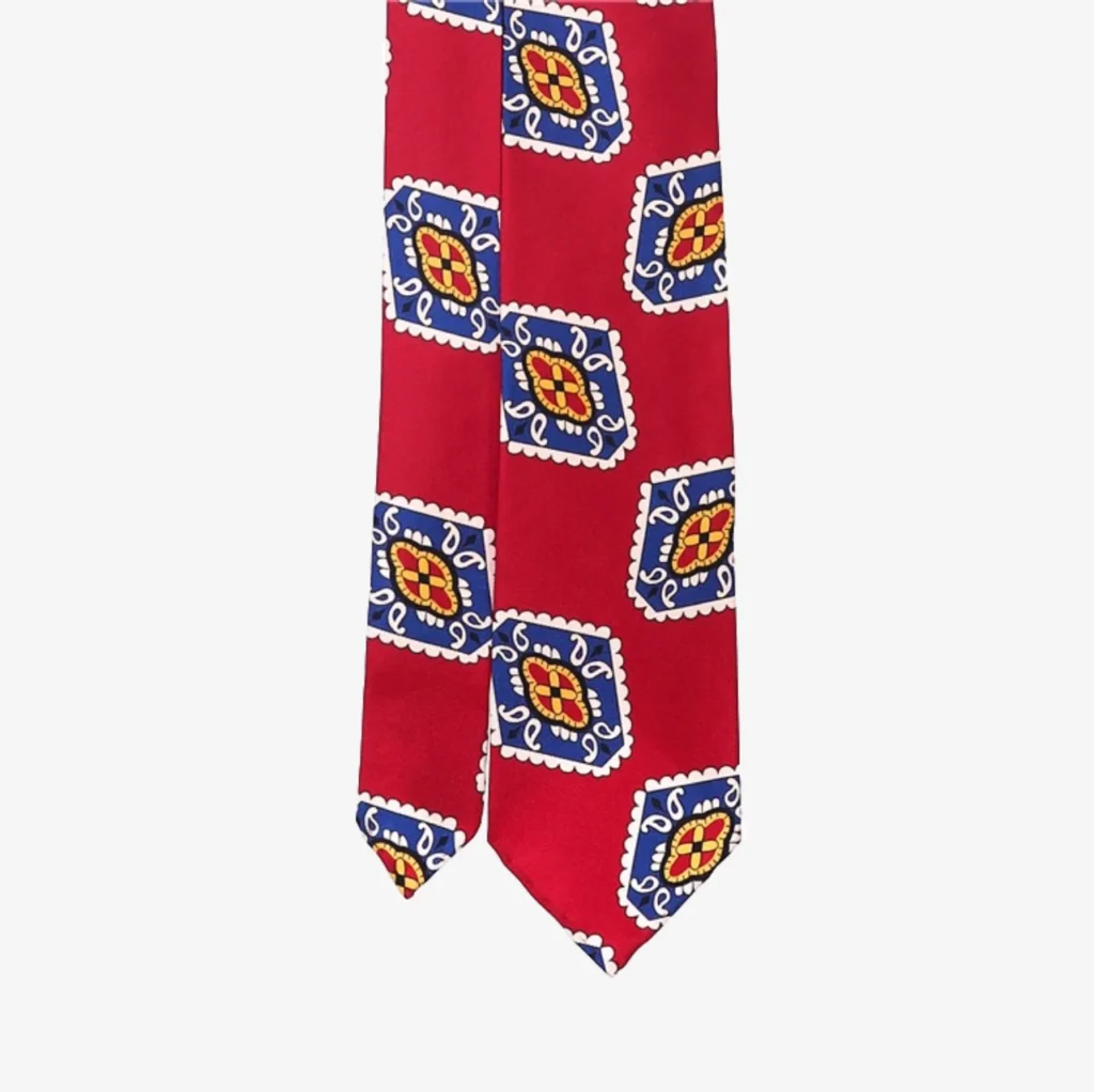 The Blue striped silk tie – Brown (Copy) offers a vibrant alternative with its red base, blue and white square pattern, and yellow-red geometric accents inside each square.