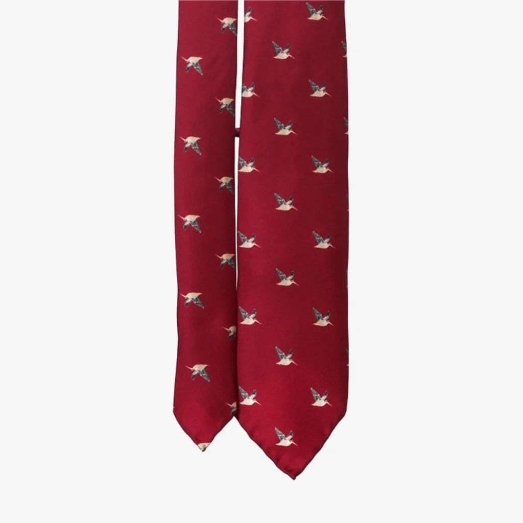 A blue geometric floral silk tie, perfect for pairing with a red necktie featuring small flying duck illustrations for a sophisticated and playful touch.
